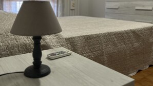 Een slaapkamer met een bed, een nachtkastje met een lamp, een afstandsbediening en een airconditioning aan de muur.