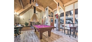 A billiards room with a pool table, wooden ceiling, stone pillar, and dining area with chairs and tables. - Mountain Cabin in Pocono Resort (Gouldsboro)