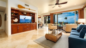 Ein geräumiges Wohnzimmer mit großem Fernseher, Holzausbau, Deckenventilator und Blick aufs Meer.