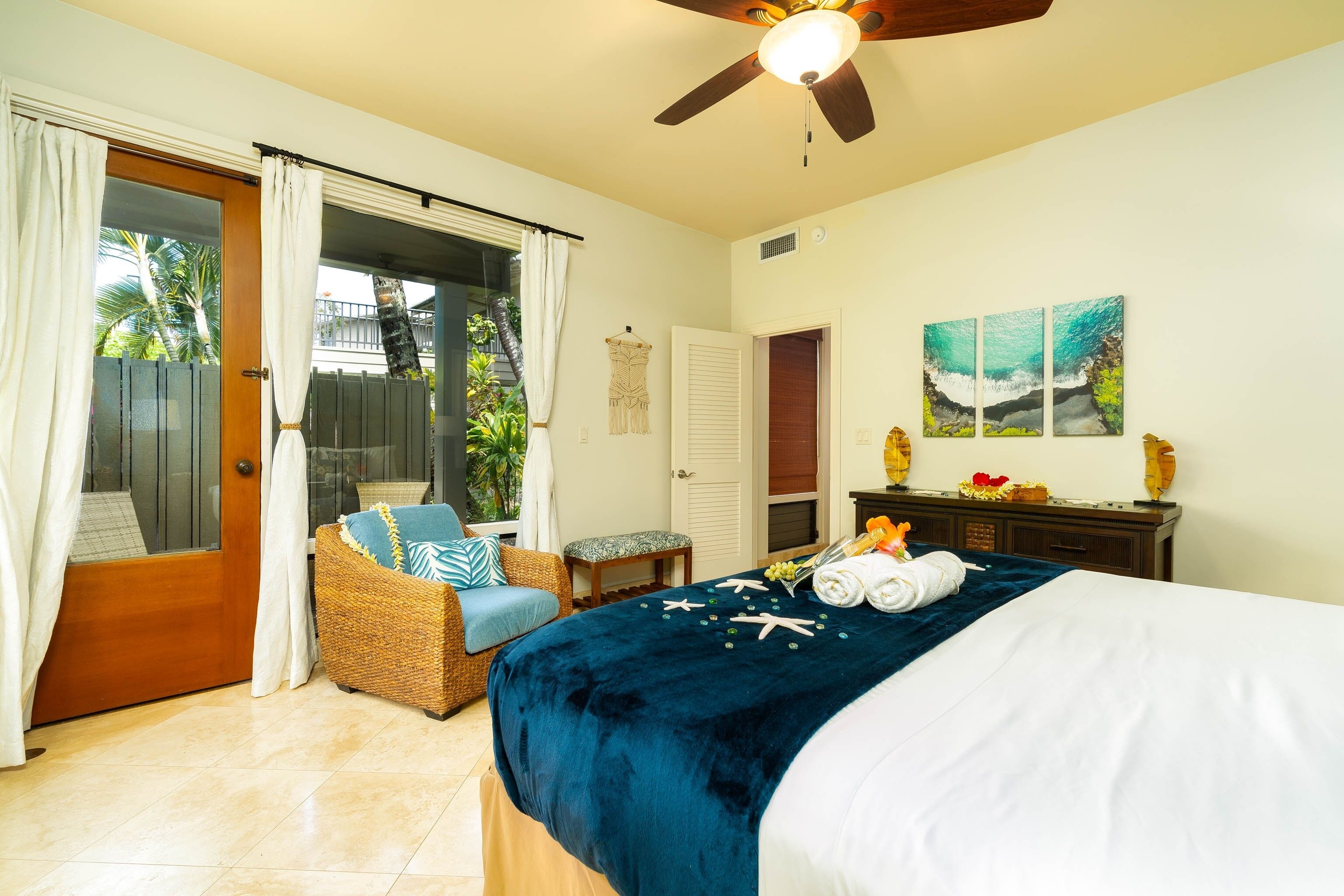 Une chambre à coucher avec un lit, une chaise en osier, une petite table et un ventilateur de plafond.