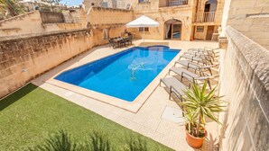 A swimming pool with lounge chairs, a table, and a potted plant. - Centre Island Gozitan Farmhouse & Pool (Kercem)