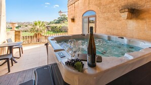 A hot tub with a bottle and grapes, a table with chairs, and a view of the landscape. - Centre Island Gozitan Farmhouse & Pool (Kercem)