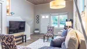 Uma sala de estar com televisão, cadeiras estampadas, sofá e janela com vista.