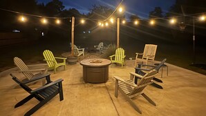 Um pátio externo com cadeiras Adirondack, um braseiro e luzes de corda.