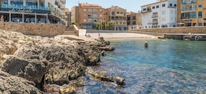 A coastal area with rocky terrain, clear water, and buildings with balconies.