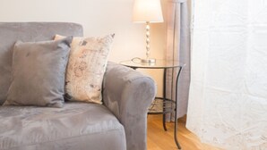 A grey sofa with patterned cushions, a small round table with a lamp, and a curtain in a room. - Cittadella Apartment (Florence)