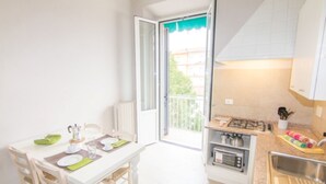 A small kitchen with a dining table, chairs, a stove, a microwave, and a balcony with a view. - Cittadella Apartment (Florence)