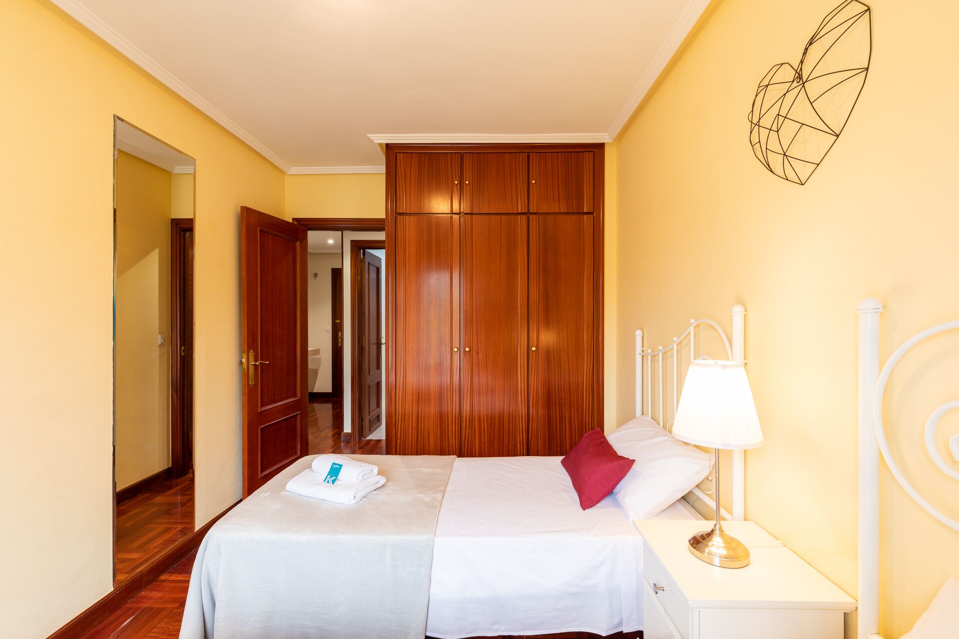 A hotel room with two beds, wooden wardrobe, white nightstands, and a wall decoration.