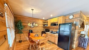 Cocina con paneles de madera, una mesa de comedor, sillas, un refrigerador y un reloj en la pared.
