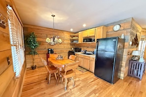 Cucina con rivestimenti in legno, un tavolo da pranzo, sedie, un frigorifero e una sveglia appesa al muro.