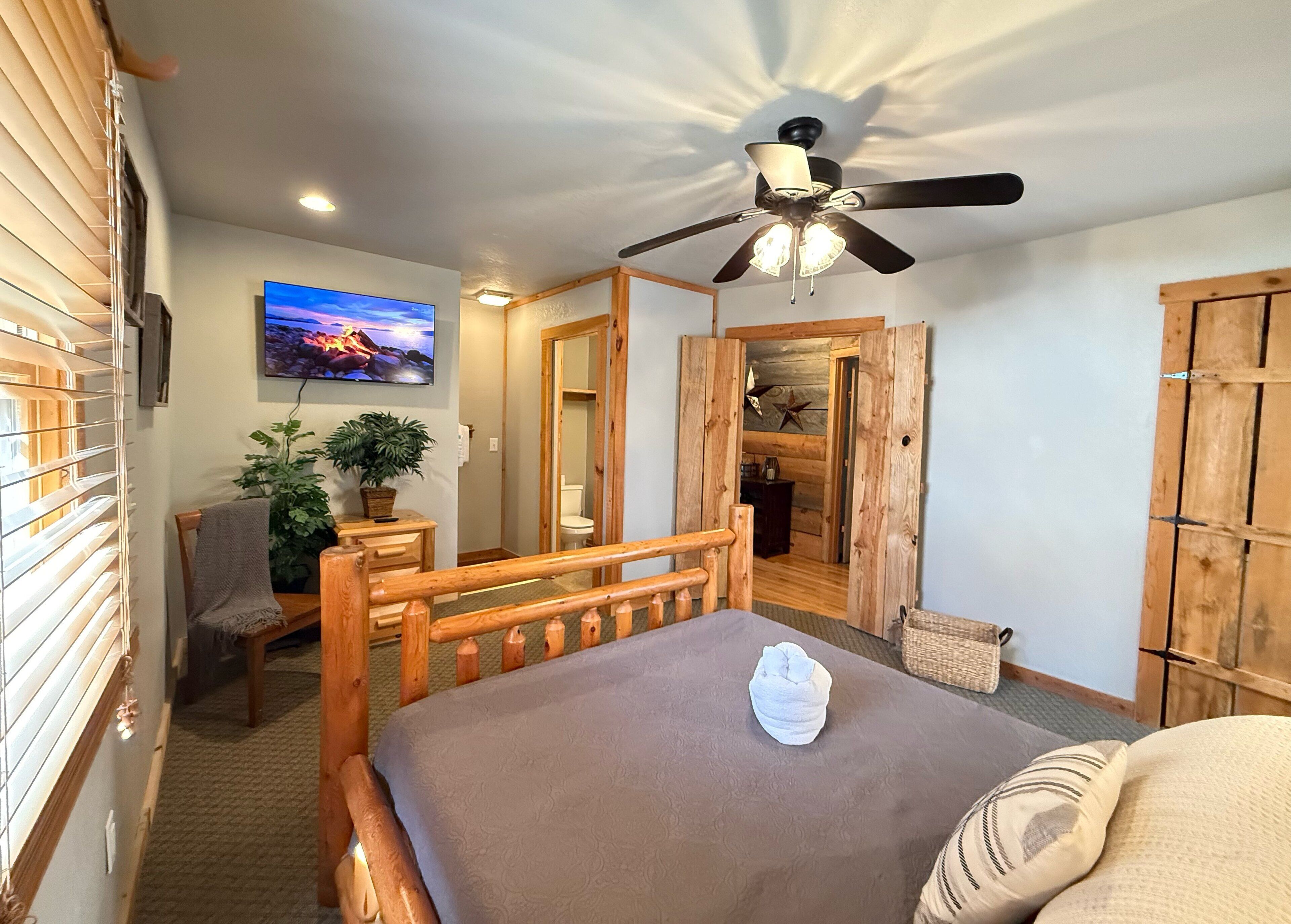 Une chambre à coucher avec un lit en bois, un ventilateur de plafond, une télévision, une plante et une armoire en bois.