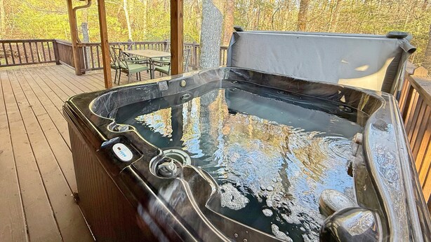 Un jacuzzi en una terraza de madera con vistas a árboles.