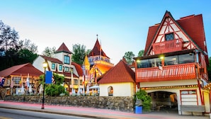 A row of traditional European-style buildings with steep roofs and colorful facades, a stone wall, and a paved street with a pedestrian walkway.