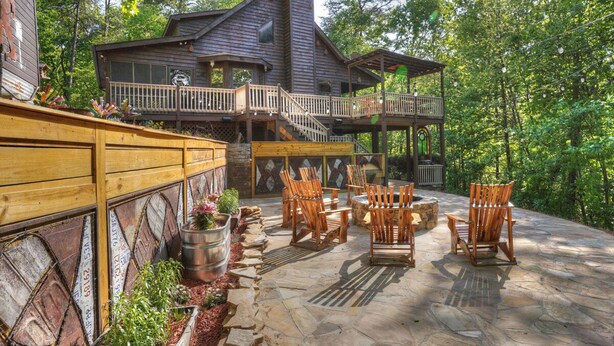 A wooden cabin with a stone patio, outdoor seating, and a balcony.