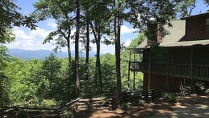 Une cabane dotée d’un balcon, entourée de grands arbres et offrant une vue sur les montagnes.
