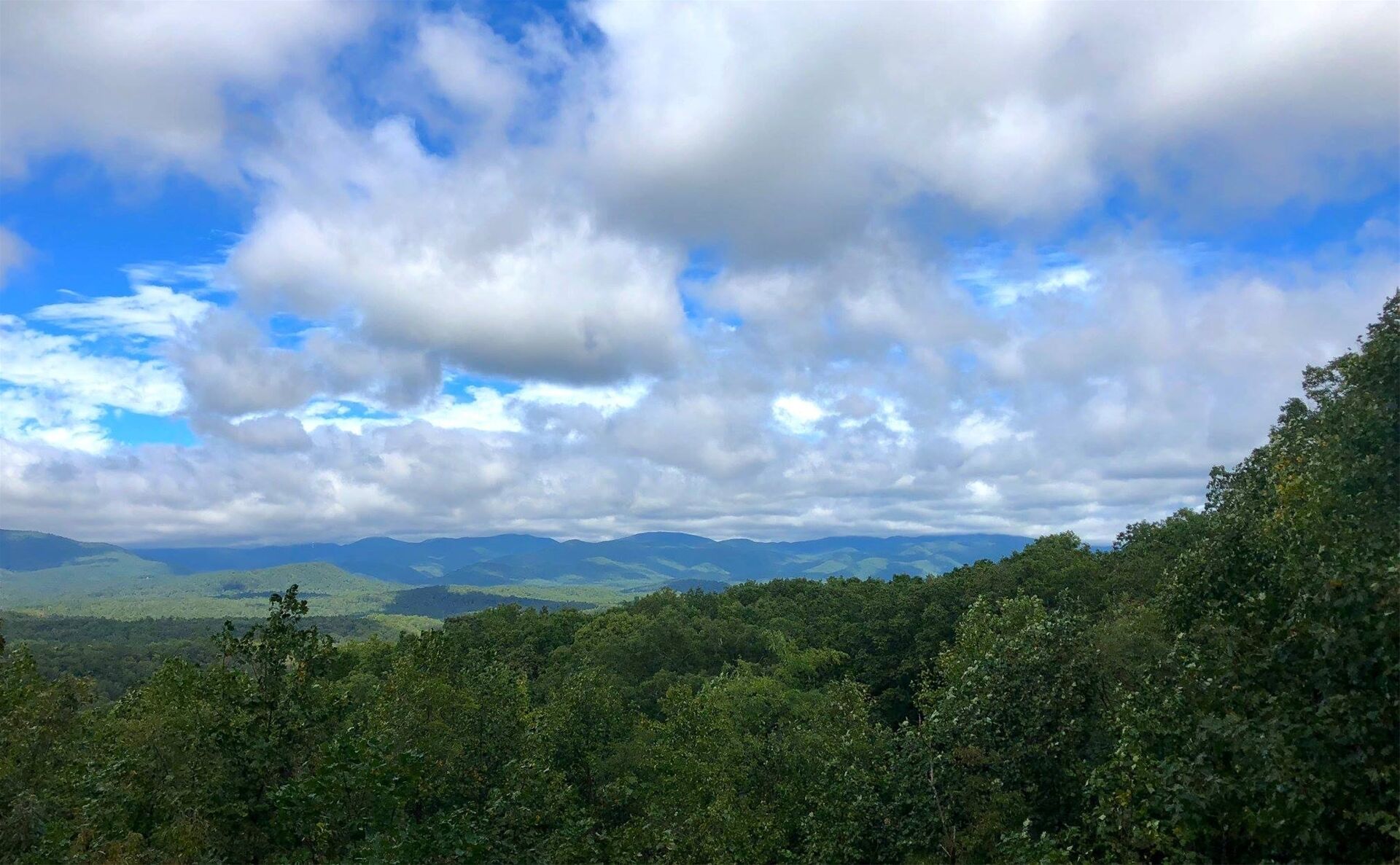 A mountainous landscape with dense forest and a partly cloudy sky.
