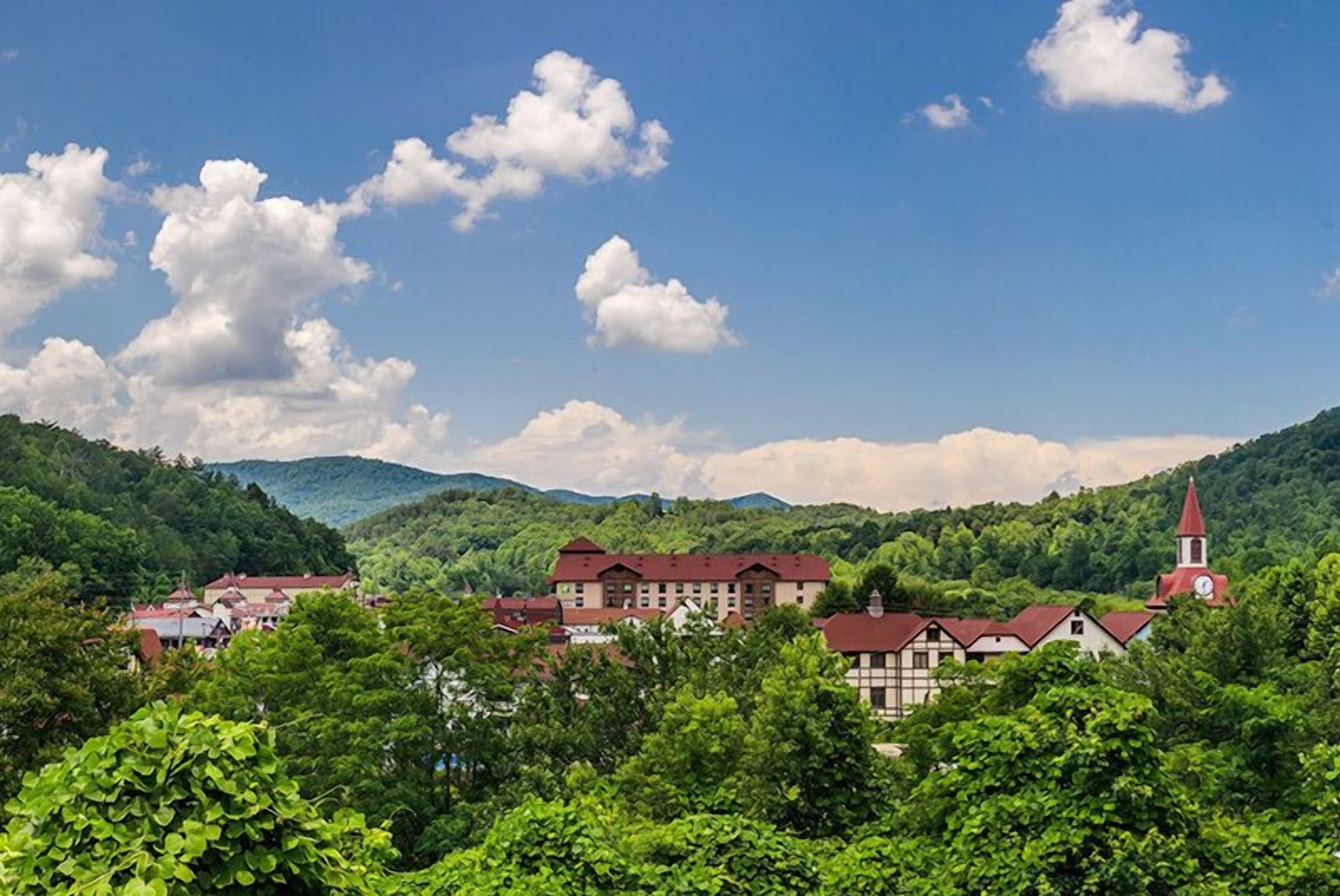 A traditional European village with red-roofed buildings, a church with a steeple, and lush green hills in the background.