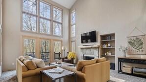 A spacious living room with large windows, a fireplace, and a television. - Relaxing Retreat - Close to Downtown Harbor Springs and Ski Resorts! (Harbor Springs)