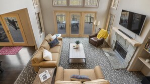 A spacious living room with a large TV, fireplace, and a view of the deck through large windows. - Relaxing Retreat - Close to Downtown Harbor Springs and Ski Resorts! (Harbor Springs)