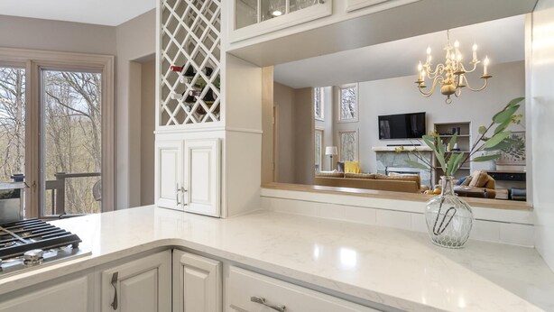 A modern kitchen with white cabinetry, a built-in stove, and a large island. There is a chandelier above the island and a vase with flowers on the countertop. - Relaxing Retreat - Close to Downtown Harbor Springs and Ski Resorts! (Harbor Springs)