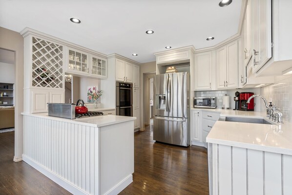 Cocina moderna con armarios blancos, un refrigerador de acero inoxidable y una isla central con un hervidor rojo.