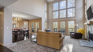 A spacious living room with a large window, a fireplace, and a dining area visible through an open door. - Relaxing Retreat - Close to Downtown Harbor Springs and Ski Resorts! (Harbor Springs)