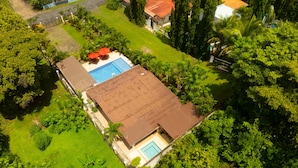 An aerial view of a property with a swimming pool, a covered patio, and lush greenery.