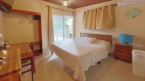 A bedroom with a bed, a wooden dresser, a table, and a window with curtains.