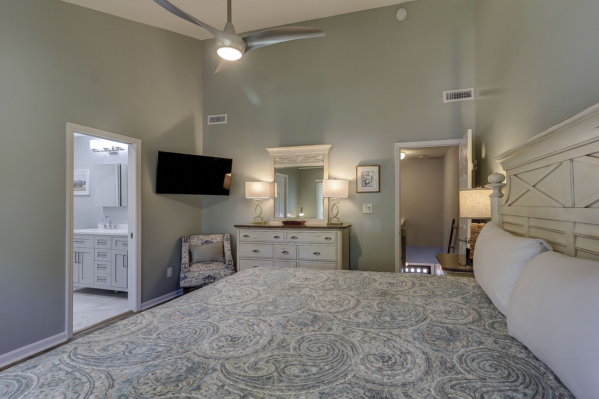 A bedroom with a bed, a dresser, a chair, a television, and a ceiling fan.