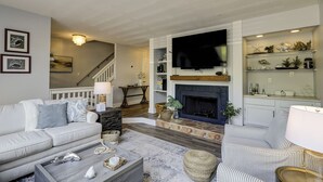 Ein Wohnzimmer mit Kamin, Fernseher und einer Treppe, die in eine andere Ebene führt.