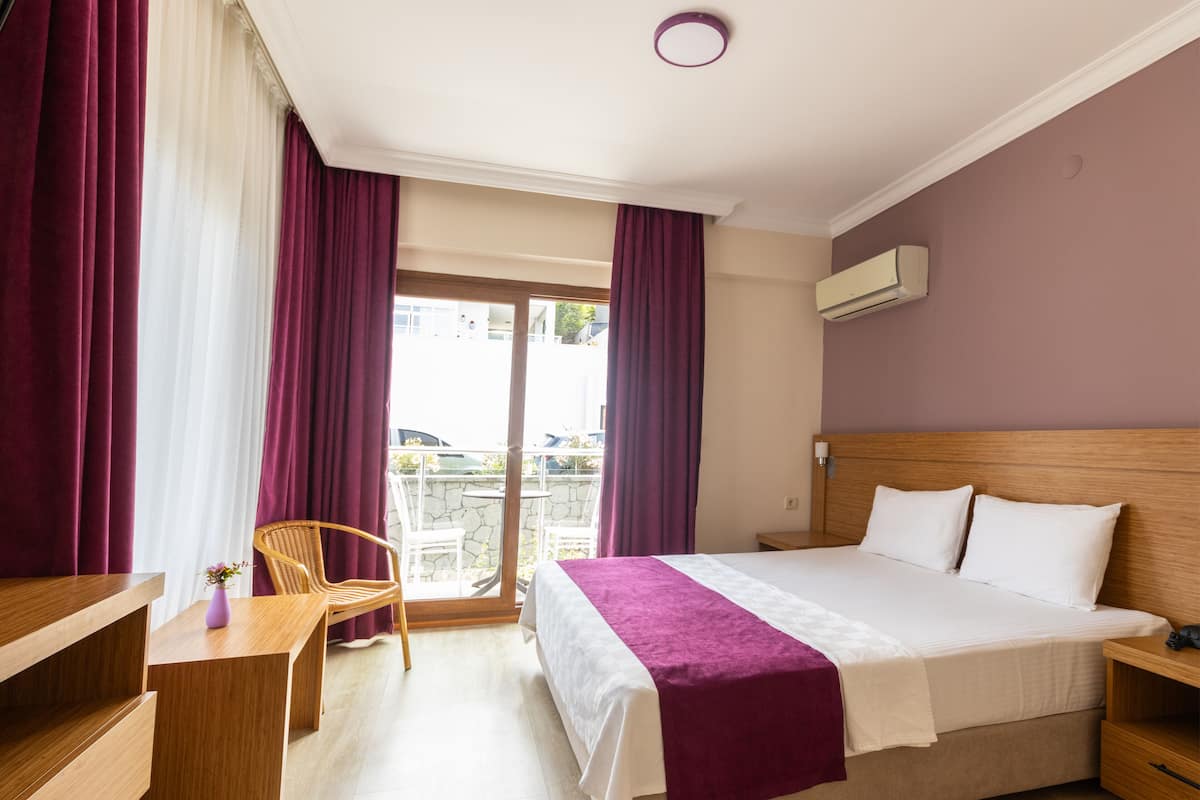 Habitación de hotel con cama, escritorio, silla y balcón con vistas.
