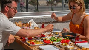 A dining table with various dishes and a person eating. - Siriusmi hotel (Cesme)