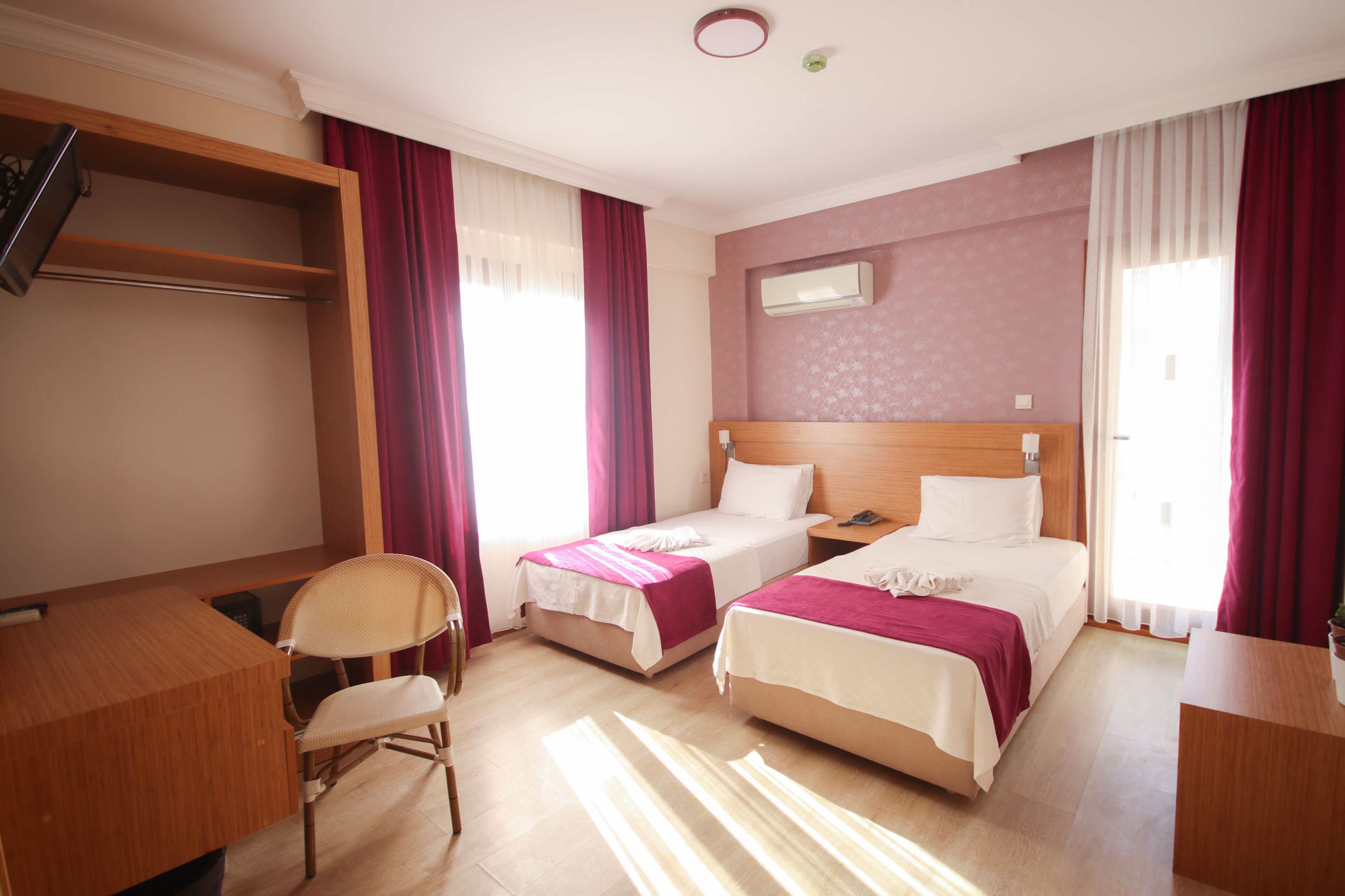 A hotel room with two single beds, a desk, a chair, and a wardrobe.
