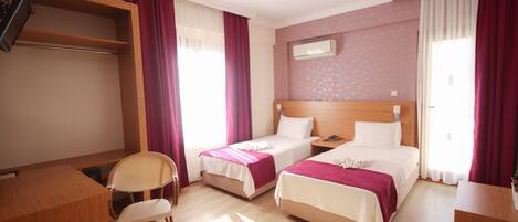 A hotel room with two single beds, a desk, a chair, and a wardrobe.