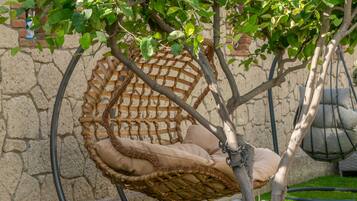 A hanging chair attached to a tree in a garden area with a stone wall in the background.