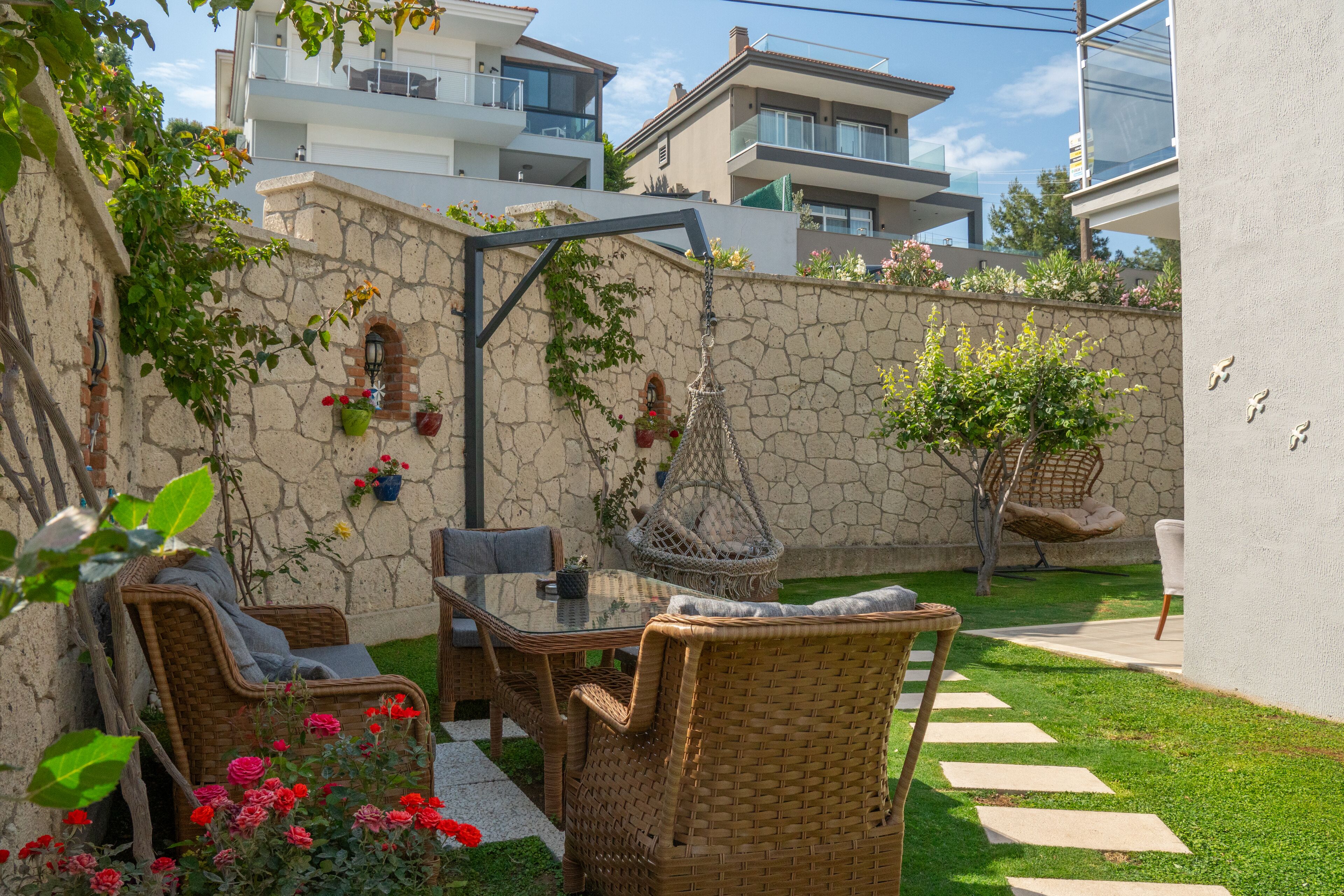 A patio with wicker furniture, a hanging chair, and a stone wall.