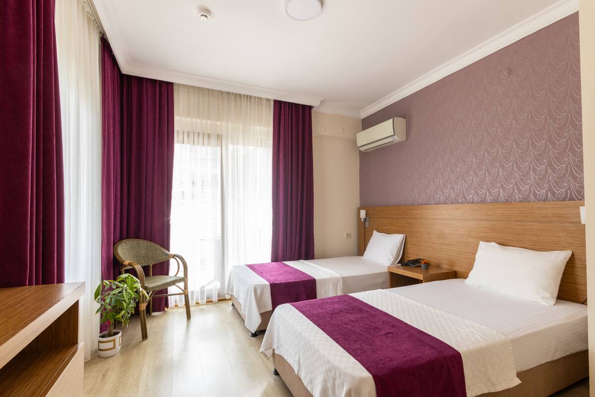 Habitación de hotel con dos camas, un cabecero de madera, una silla, una mesita y una planta en maceta.