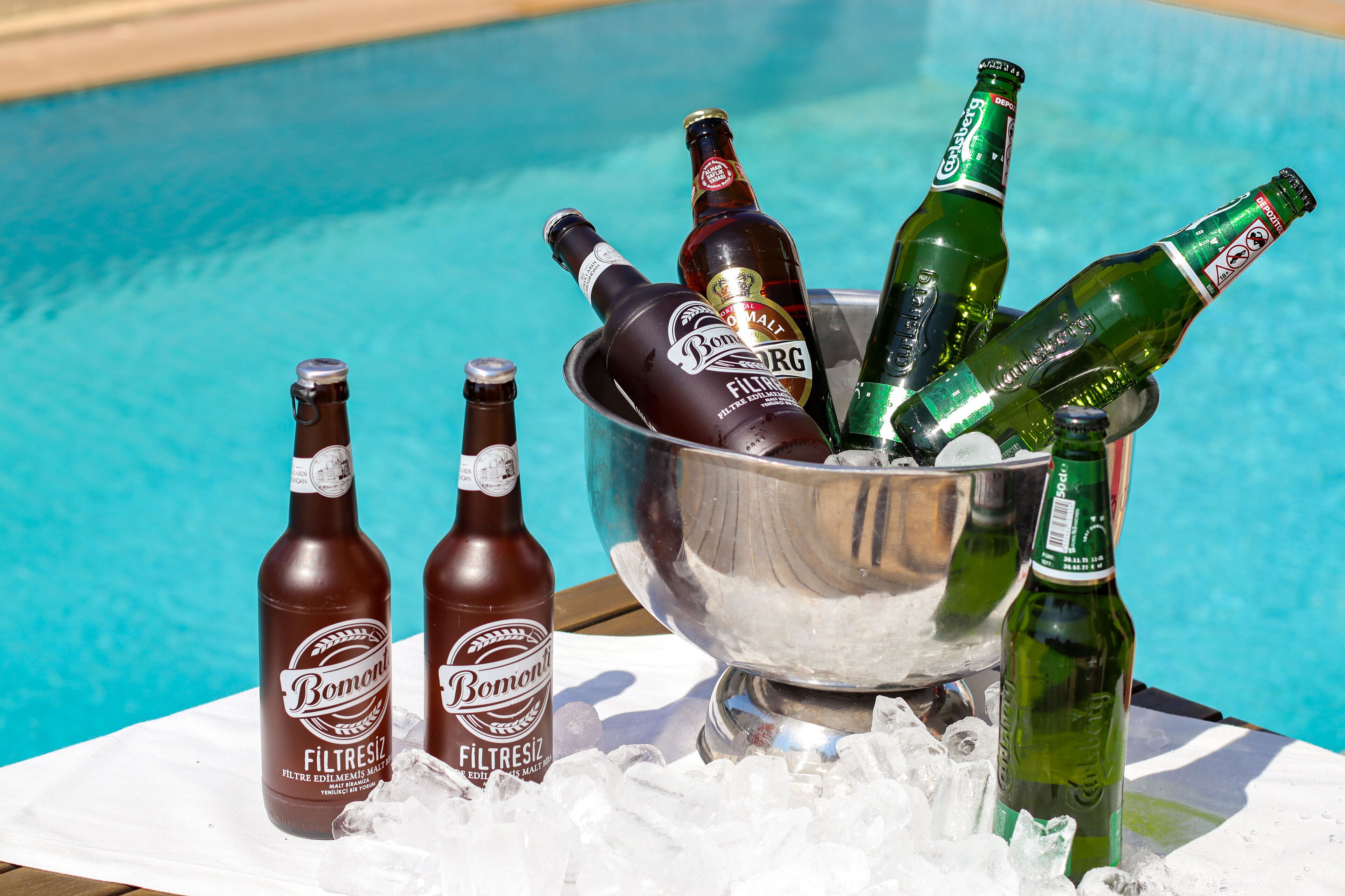 A poolside setting with bottles of beer in a metal bucket.