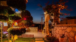 A well-lit outdoor area with a stone wall, a wooden fence, and various potted plants. - Siriusmi hotel (Cesme)