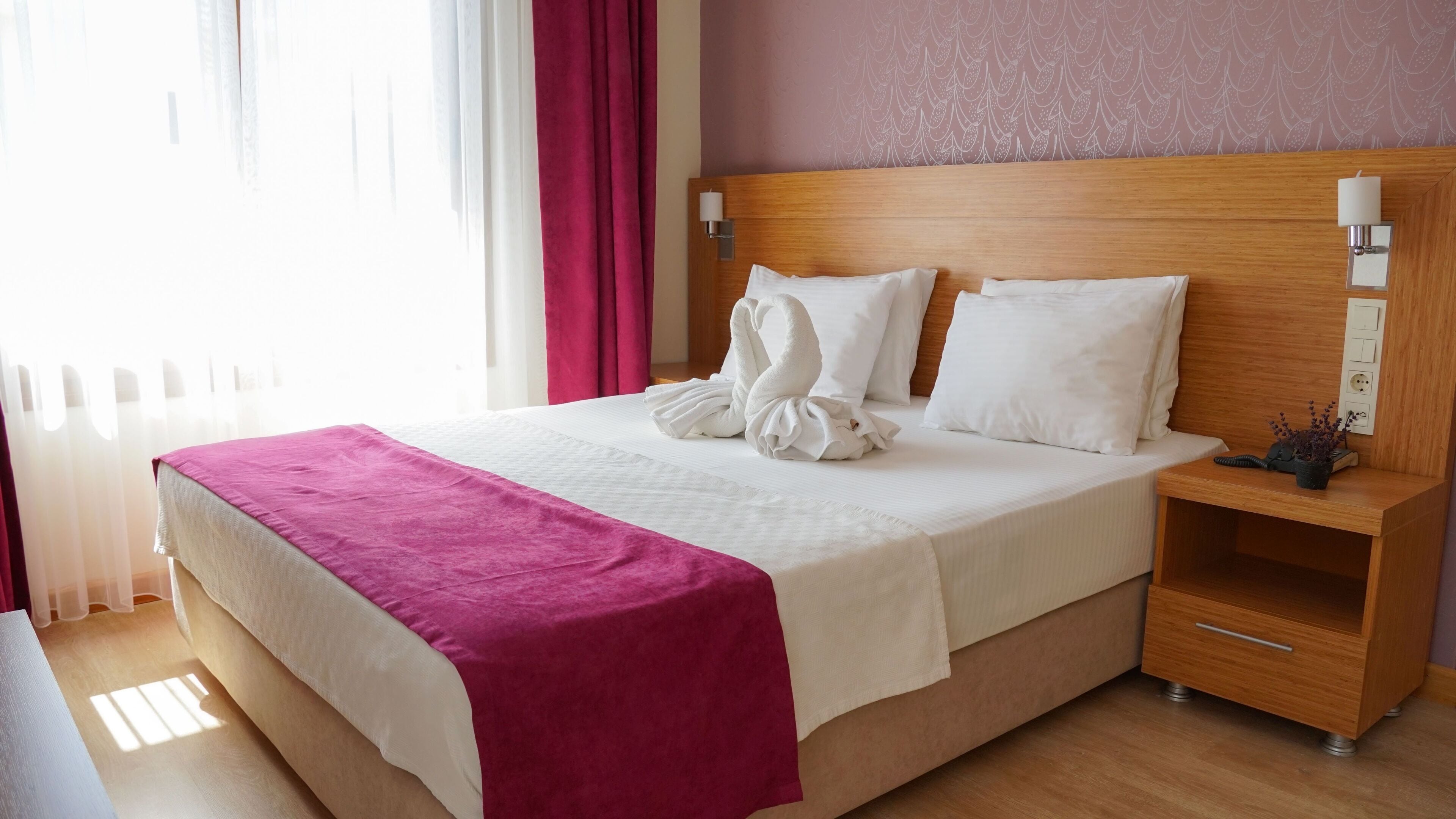 Una cama bien hecha con un cubrecolor rosa, almohadas blancas y un cabecero de madera.