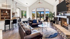 A spacious living area with a stone fireplace, leather sofa, and a dining area with a kitchen in the background. - The Bentley Estate: Festivals, Karaoke, Grotto, Sauna, Putting Green, BBQ! (Bermuda Dunes)
