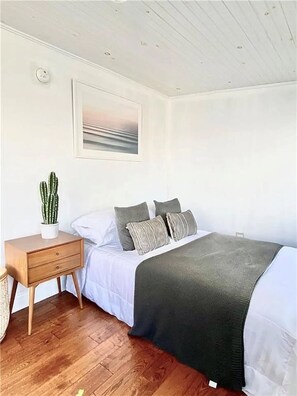 A bedroom with a bed, a nightstand, a cactus, and a painting on the wall.