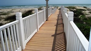 A wooden boardwalk leading to a beach with white railings. - Sea Pointer Inn - Private Beach House With Pool 3 Bedroom Home by RedAwning (South Padre Island)