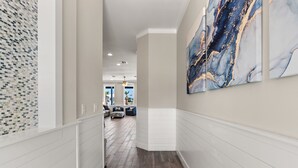 A hallway with white paneling, a wooden floor, and a large abstract painting on the right wall. - Sea Pointer Inn - Private Beach House With Pool 3 Bedroom Home by RedAwning (South Padre Island)
