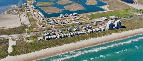Vue aérienne d’une station balnéaire comprenant plusieurs bâtiments, une plage et un port de plaisance.