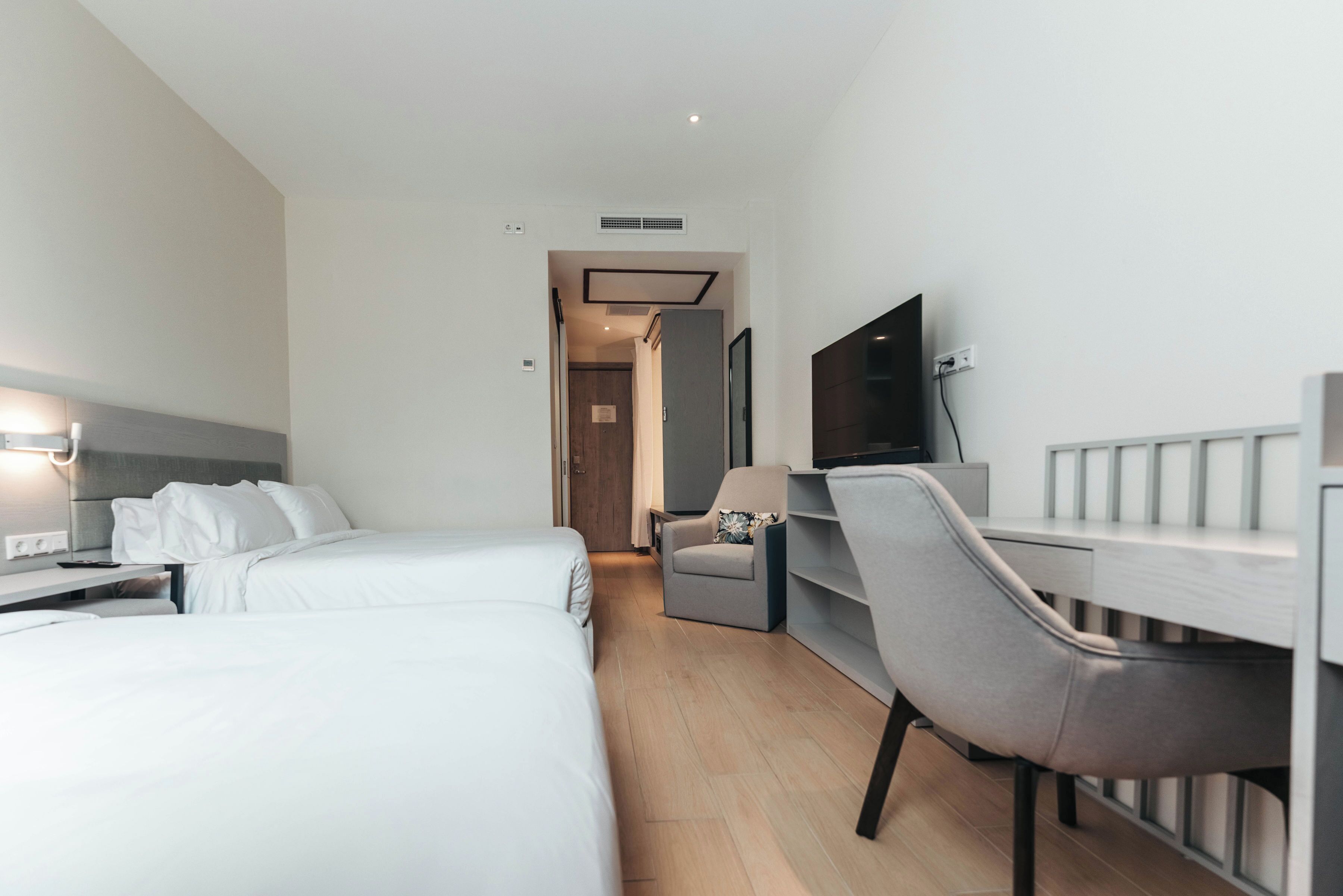A hotel room with two beds, a desk, a chair, a TV, and a wardrobe.