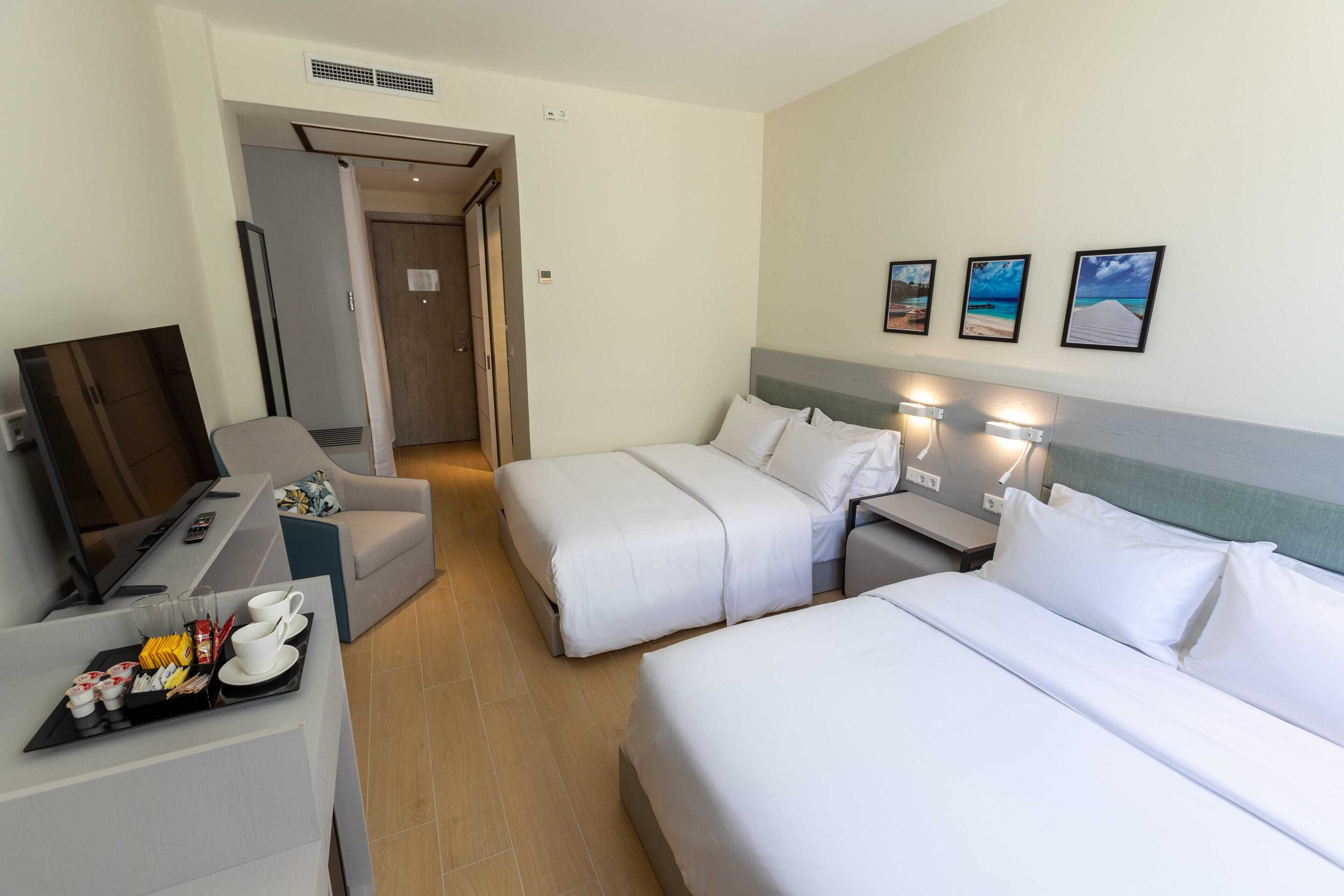 Camera d'albergo con due letti, una scrivania e un vassoio con prodotti per la colazione, e un televisore.