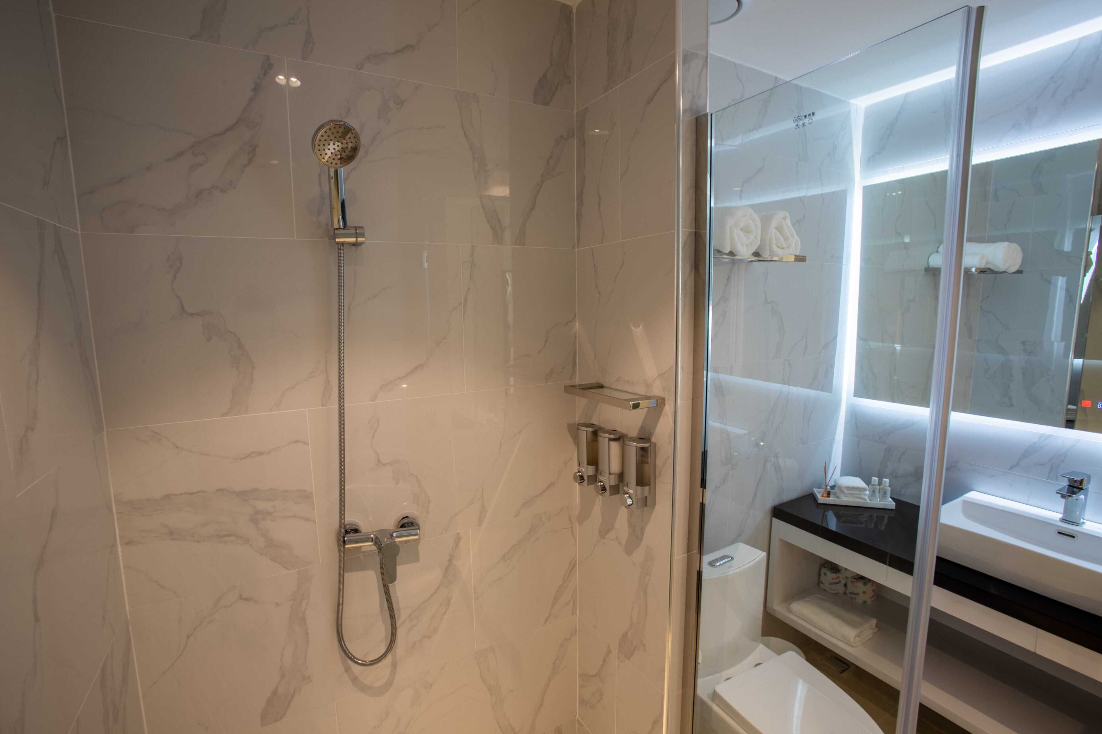 Un baño moderno con ducha envuelta en vidrio, baldosas de mármol, lavamanos con encimera negra y puerta de cristal para la ducha.