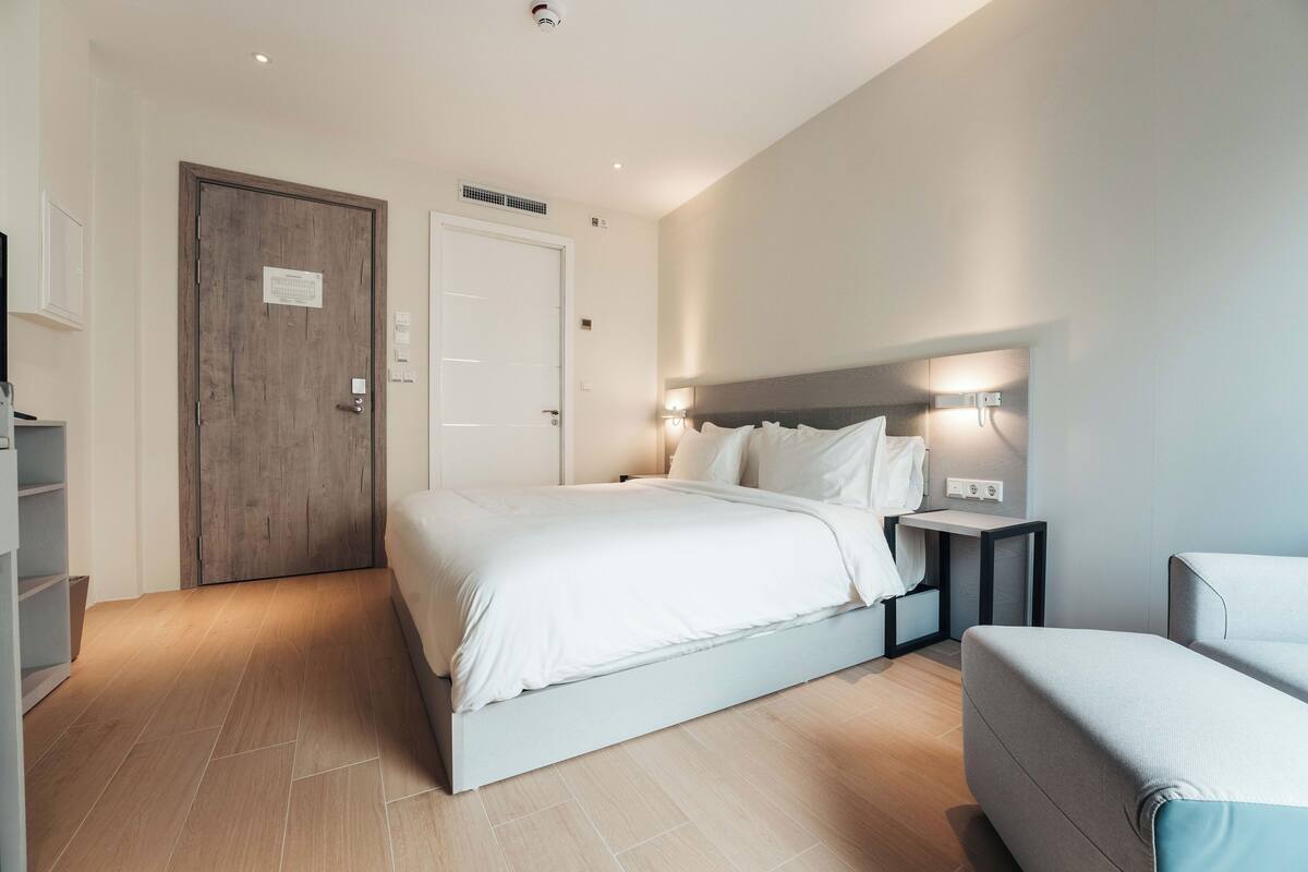A modern hotel room with a large bed, bedside tables, a wardrobe, and a seating area.