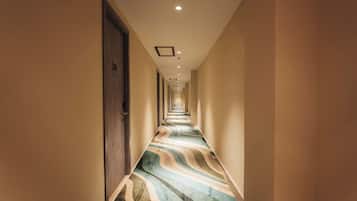 Corredor de hotel com carpete estampado, portas em ambos os lados e iluminação embutida no teto.